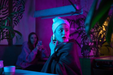 İnci küpeli güzel bir kız modern kafede öğle yemeği yiyor, neon ışıklı bir restoranda.