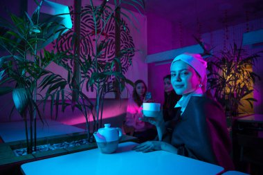 İnci küpeli güzel bir kız modern kafede öğle yemeği yiyor, neon ışıklı bir restoranda.