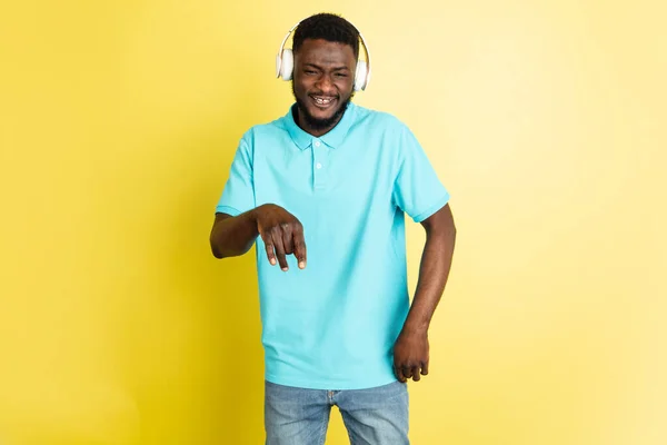 Joven hombre africano en auriculares aislados sobre fondo de estudio amarillo con copyspace. — Foto de Stock