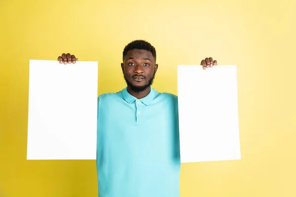 Joven africano con hojas de papel en blanco aisladas sobre fondo amarillo del estudio. —  Fotos de Stock