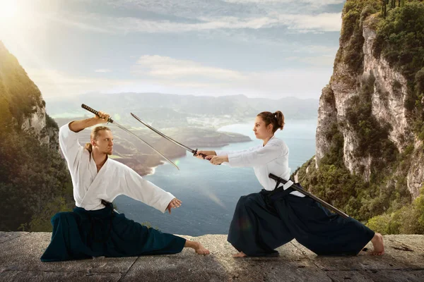 Man and woman, teacher fighting Aikido, training martial arts on meadow in front of lake and mountains