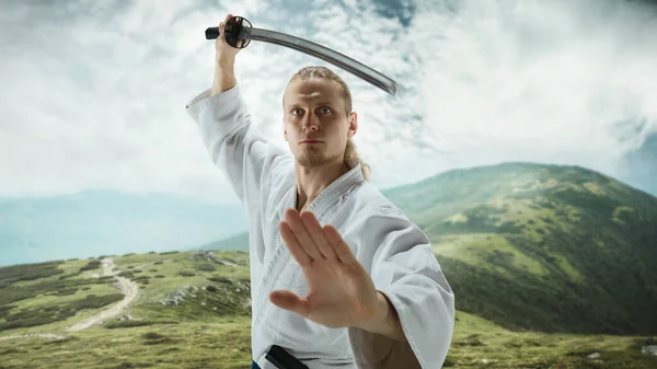 Young man, teacher fighting Aikido, training martial arts on meadow in front mountains