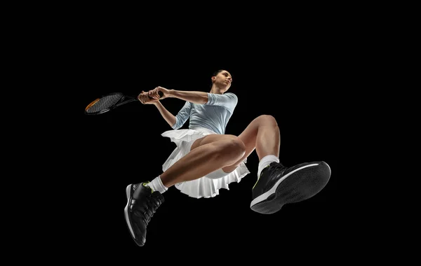 Jogadora de tênis profissional em ação, movimento isolado em fundo preto, olhar de baixo. Conceito de esporte, movimento, energia e dinâmica. — Fotografia de Stock