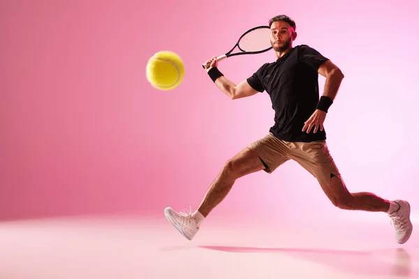 Giovane uomo caucasico che gioca a tennis isolato su sfondo rosa studio, azione e movimento concetto — Foto Stock