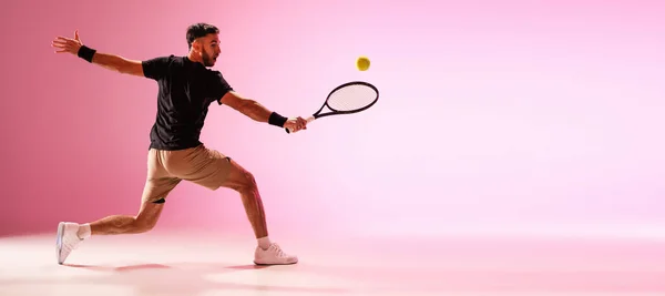 Joven hombre caucásico jugando al tenis aislado sobre fondo de estudio rosa, acción y concepto de movimiento —  Fotos de Stock