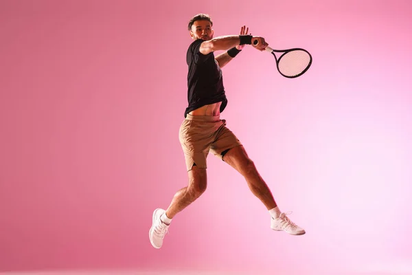 Mladý běloch hraje tenis izolovaný na růžovém pozadí studia, akční a pohybový koncept — Stock fotografie