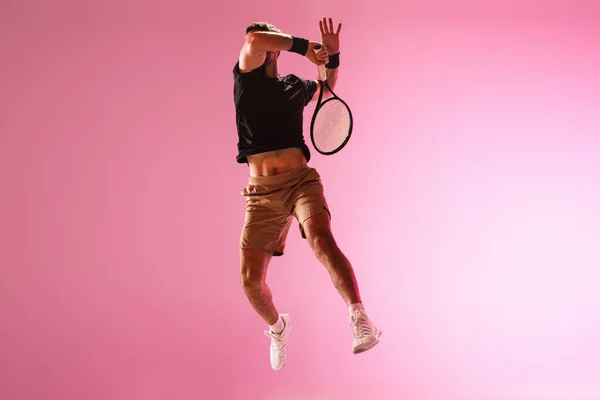 Joven hombre caucásico jugando al tenis aislado sobre fondo de estudio rosa, acción y concepto de movimiento — Foto de Stock