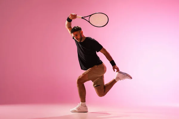 Joven hombre caucásico jugando al tenis aislado sobre fondo de estudio rosa, acción y concepto de movimiento — Foto de Stock