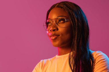 Neon rengi pembe stüdyo arka planında Afrikalı genç kadın portresi. İnsan duyguları kavramı, yüz ifadesi, gençlik, satış, reklam.