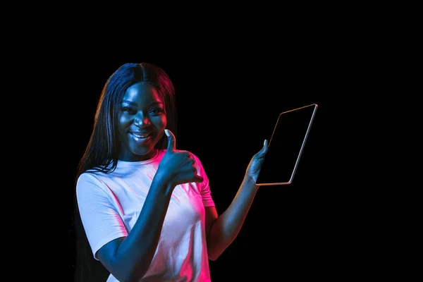 Afrikaanse jonge vrouwen portret op donkere studio achtergrond in neon. Concept van menselijke emoties, gezichtsuitdrukking, jeugd, verkoop, reclame. — Stockfoto