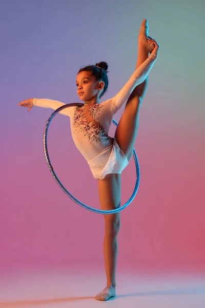 Afroamerikansk rytmisk gymnast, söt flicka öva på lutning studio bakgrund i neon ljus — Stockfoto