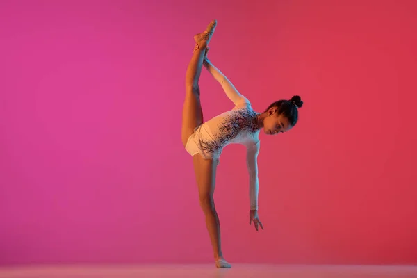 Africano-americano ginasta rítmica, menina bonita praticando no fundo do estúdio gradiente em luz de néon — Fotografia de Stock