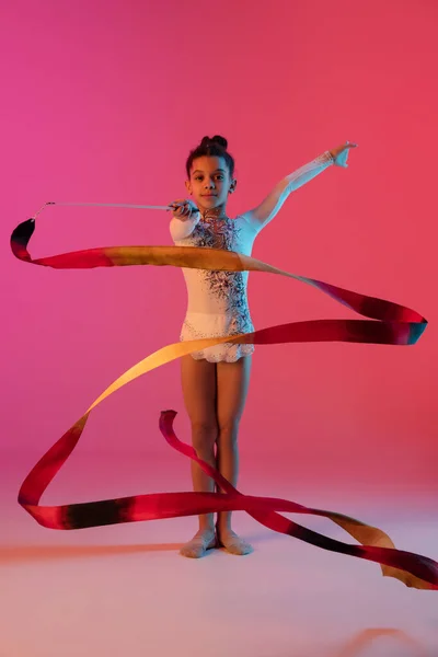 Afroamerikansk rytmisk gymnast, söt flicka öva på lutning studio bakgrund i neon ljus — Stockfoto