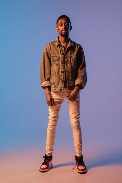 Homem elegante jovem em roupa de estilo moderno rua isolado no fundo gradiente em luz de néon. Modelo na moda afro-americano em livro de visual, músico realizando. — Fotografia de Stock