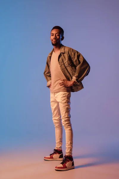 Homem elegante jovem em roupa de estilo moderno rua isolado no fundo gradiente em luz de néon. Modelo na moda afro-americano em livro de visual, músico realizando. — Fotografia de Stock