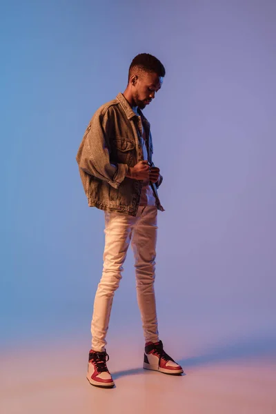 穿着现代街道风格服装的年轻时尚男子在霓虹灯下被隔离在渐变的背景下。非洲裔美国人流行模特在相册，音乐家表演. — 图库照片