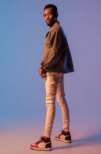 Молодой стильный мужчина в современном уличном костюме изолирован на градиентном фоне в неоновом свете. Африканско-американская модная модель в глянцевой книге, музыкант выступает. — стоковое фото