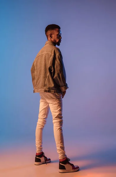 Fiatal elegáns férfi modern utcai stílusú ruhát elszigetelt gradiens háttér neon fény. Afrikai-amerikai divatos modell megjelenés könyv, zenész előadó. — Stock Fotó