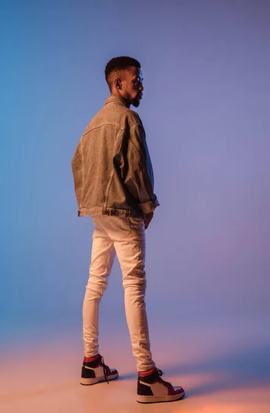 Homem elegante jovem em roupa de estilo moderno rua isolado no fundo gradiente em luz de néon. Modelo na moda afro-americano em livro de visual, músico realizando. — Fotografia de Stock