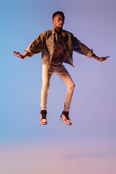 Hombre joven y elegante en traje de estilo urbano moderno aislado sobre fondo degradado en luz de neón. modelo de moda afroamericana en el libro de la mirada, músico que realiza. — Foto de Stock