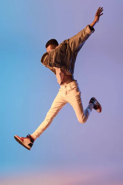 Jonge stijlvolle man in moderne straat stijl outfit geïsoleerd op gradiënt achtergrond in neon licht. Afro-Amerikaanse modieuze model in look boek, muzikant uitvoeren. — Stockfoto