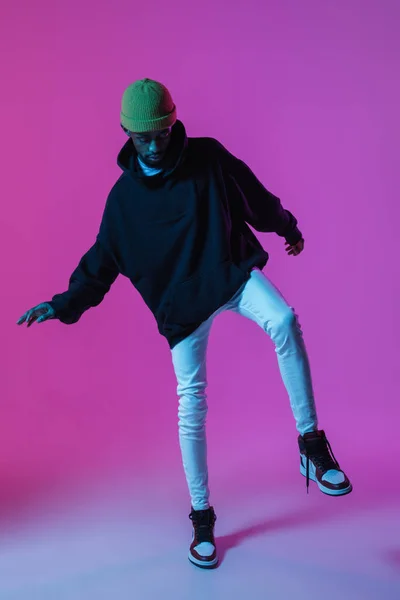 Młody, stylowy mężczyzna w nowoczesnym stroju ulicznym, odizolowany na gradientowym tle w neonowym świetle. Afroamerykanin modny model w książce wyglądu, muzyk występujący. — Zdjęcie stockowe
