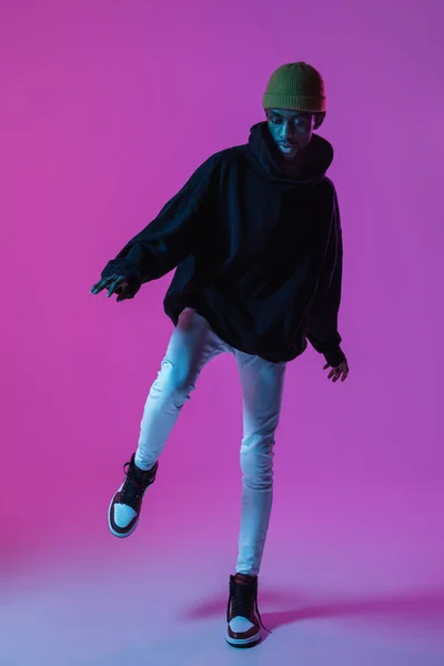 穿着现代街道风格服装的年轻时尚男子在霓虹灯下被隔离在渐变的背景下。非洲裔美国人流行模特在相册，音乐家表演. — 图库照片