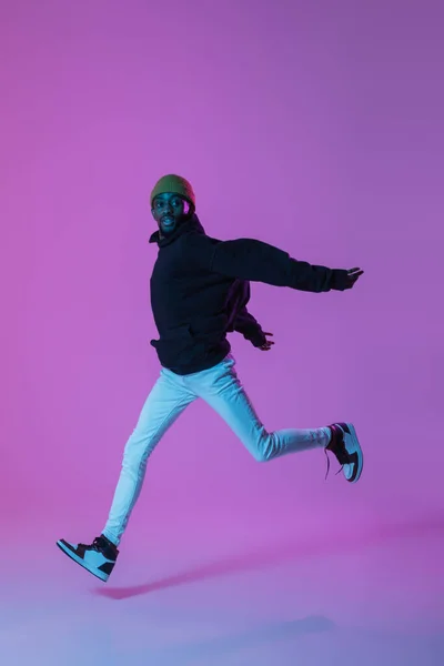 Hombre joven y elegante en traje de estilo urbano moderno aislado sobre fondo degradado en luz de neón. modelo de moda afroamericana en el libro de la mirada, músico que realiza. — Foto de Stock