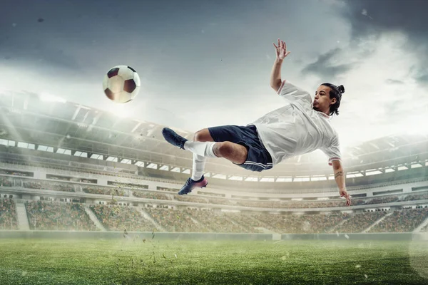 Football masculin, joueur de football attrapant le ballon dans le saut au stade pendant le match de sport sur fond de ciel sombre — Photo