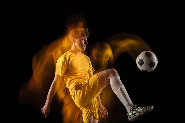 Jonge Kaukasische mannelijke voetbal of voetballer schoppen bal voor het doel in gemengd licht op donkere achtergrond. Concept van gezonde levensstijl, professionele sport, hobby. — Stockfoto