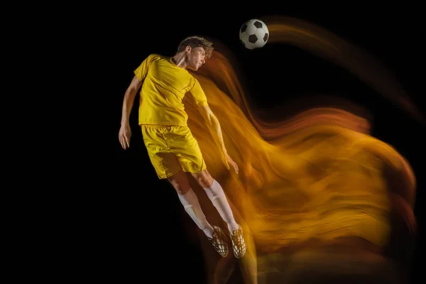 Jonge Kaukasische mannelijke voetbal of voetballer schoppen bal voor het doel in gemengd licht op donkere achtergrond. Concept van gezonde levensstijl, professionele sport, hobby. — Stockfoto