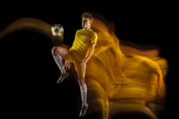 Молодий кавказький футболіст або футболіст штовхає м'яч до мети у змішаному світлі на темному тлі. Концепція здорового способу життя, професійний спорт, хобі . — стокове фото