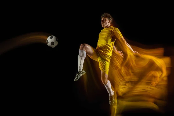 Jonge Kaukasische mannelijke voetbal of voetballer schoppen bal voor het doel in gemengd licht op donkere achtergrond. Concept van gezonde levensstijl, professionele sport, hobby. — Stockfoto