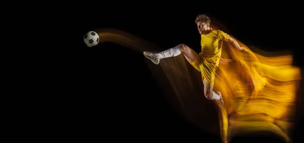 Jovem caucasiano de futebol masculino ou jogador de futebol chutando bola para o gol em luz mista sobre fundo escuro. Conceito de estilo de vida saudável, esporte profissional, hobby. — Fotografia de Stock
