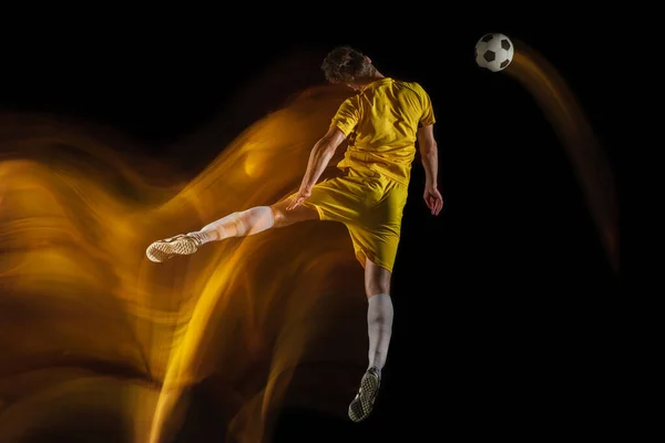 Jonge Kaukasische mannelijke voetbal of voetballer schoppen bal voor het doel in gemengd licht op donkere achtergrond. Concept van gezonde levensstijl, professionele sport, hobby. — Stockfoto