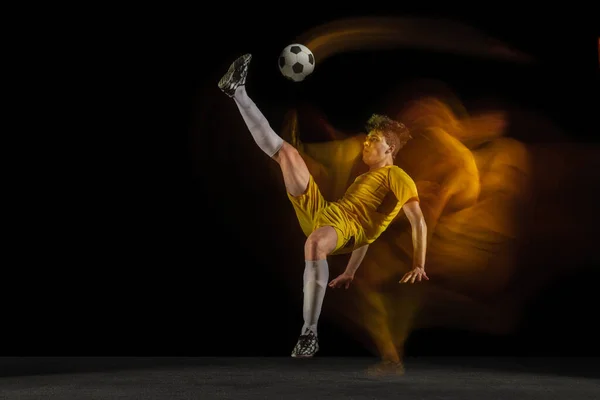 Jonge Kaukasische mannelijke voetbal of voetballer schoppen bal voor het doel in gemengd licht op donkere achtergrond. Concept van gezonde levensstijl, professionele sport, hobby. — Stockfoto