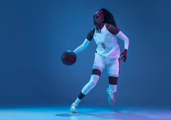 Beautiful african-american female basketball player in motion and action in neon light on blue background. Concept of healthy lifestyle, professional sport, hobby. — Stock Photo, Image