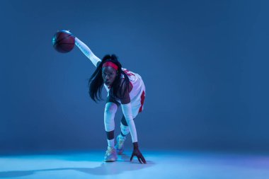 Güzel Afro-Amerikalı bayan basketbolcu mavi arka planda neon ışığı altında hareket ediyor. Sağlıklı yaşam tarzı, profesyonel spor, hobi kavramı.