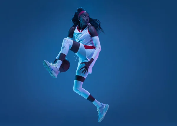 Hermosa jugadora de baloncesto afroamericana en movimiento y acción en luz de neón sobre fondo azul. Concepto de estilo de vida saludable, deporte profesional, hobby. —  Fotos de Stock