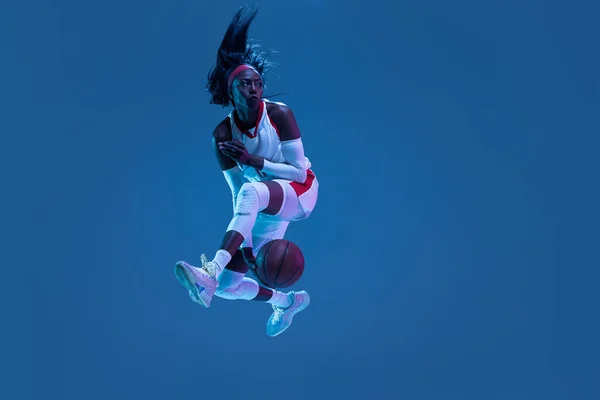 아름다운 아프리카 계 미국인 농구 선수가 푸른 배경에 네온 라이트에서 움직임 과 액션을 보여 줍니다. 건강 한 생활 방식, 직업적 인 스포츠, 취미의 개념. — 스톡 사진