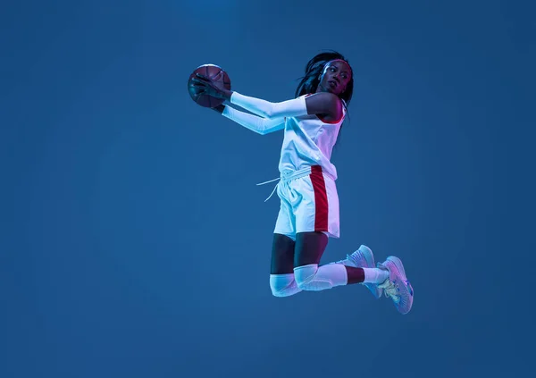 Hermosa jugadora de baloncesto afroamericana en movimiento y acción en luz de neón sobre fondo azul. Concepto de estilo de vida saludable, deporte profesional, hobby. —  Fotos de Stock