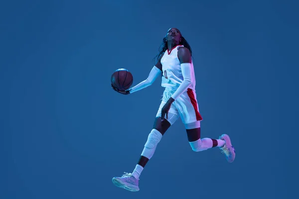 Hermosa jugadora de baloncesto afroamericana en movimiento y acción en luz de neón sobre fondo azul. Concepto de estilo de vida saludable, deporte profesional, hobby. —  Fotos de Stock