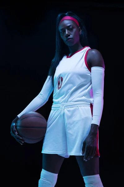 Hermosa jugadora de baloncesto afroamericana en movimiento y acción en luz de neón sobre fondo negro. Concepto de estilo de vida saludable, deporte profesional, hobby. —  Fotos de Stock