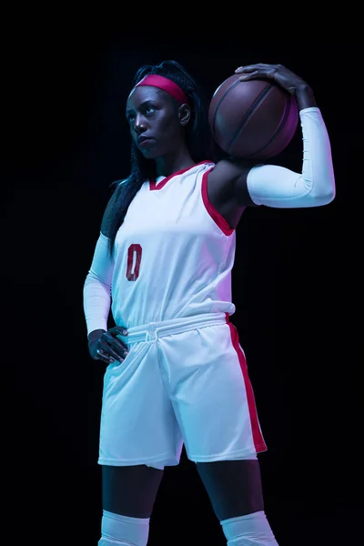 Hermosa jugadora de baloncesto afroamericana en movimiento y acción en luz de neón sobre fondo negro. Concepto de estilo de vida saludable, deporte profesional, hobby. —  Fotos de Stock