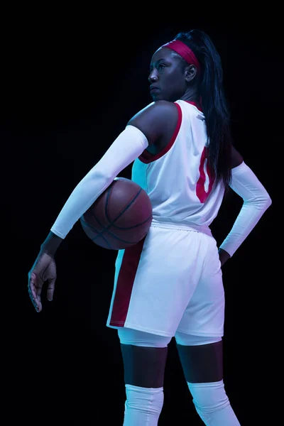 Hermosa jugadora de baloncesto afroamericana en movimiento y acción en luz de neón sobre fondo negro. Concepto de estilo de vida saludable, deporte profesional, hobby. —  Fotos de Stock