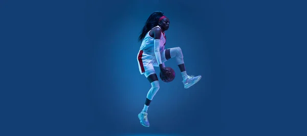 Krásná africko-americká hráčka basketbalu v pohybu a akce v neonovém světle na modrém pozadí. Koncept zdravého životního stylu, profesionální sport, hobby. — Stock fotografie