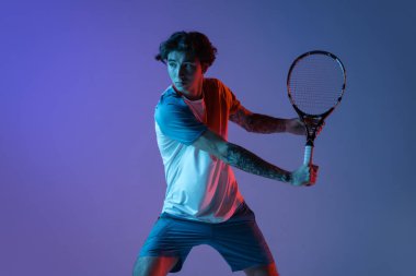 Tenis oynayan beyaz bir adam mor-mavi stüdyo arka planında, neon, aksiyon ve hareket konseptiyle izole edilmiş.