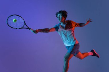 Tenis oynayan beyaz bir adam mor-mavi stüdyo arka planında, neon, aksiyon ve hareket konseptiyle izole edilmiş.