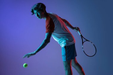 Tenis oynayan beyaz bir adam mor-mavi stüdyo arka planında, neon, aksiyon ve hareket konseptiyle izole edilmiş.
