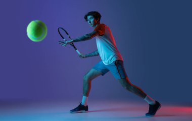 Tenis oynayan beyaz bir adam mor-mavi stüdyo arka planında, neon, aksiyon ve hareket konseptiyle izole edilmiş.